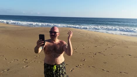 Hombre-Caucásico-En-La-Playa-Hablando-Con-Un-Teléfono-Inteligente-En-Una-Llamada-Telefónica-De-Las-Redes-Sociales-Durante-Las-Vibraciones-Del-Verano-Al-Atardecer