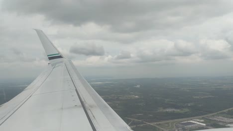 looking out the airplane over the wing as the plane gains altitude and passes through the clouds