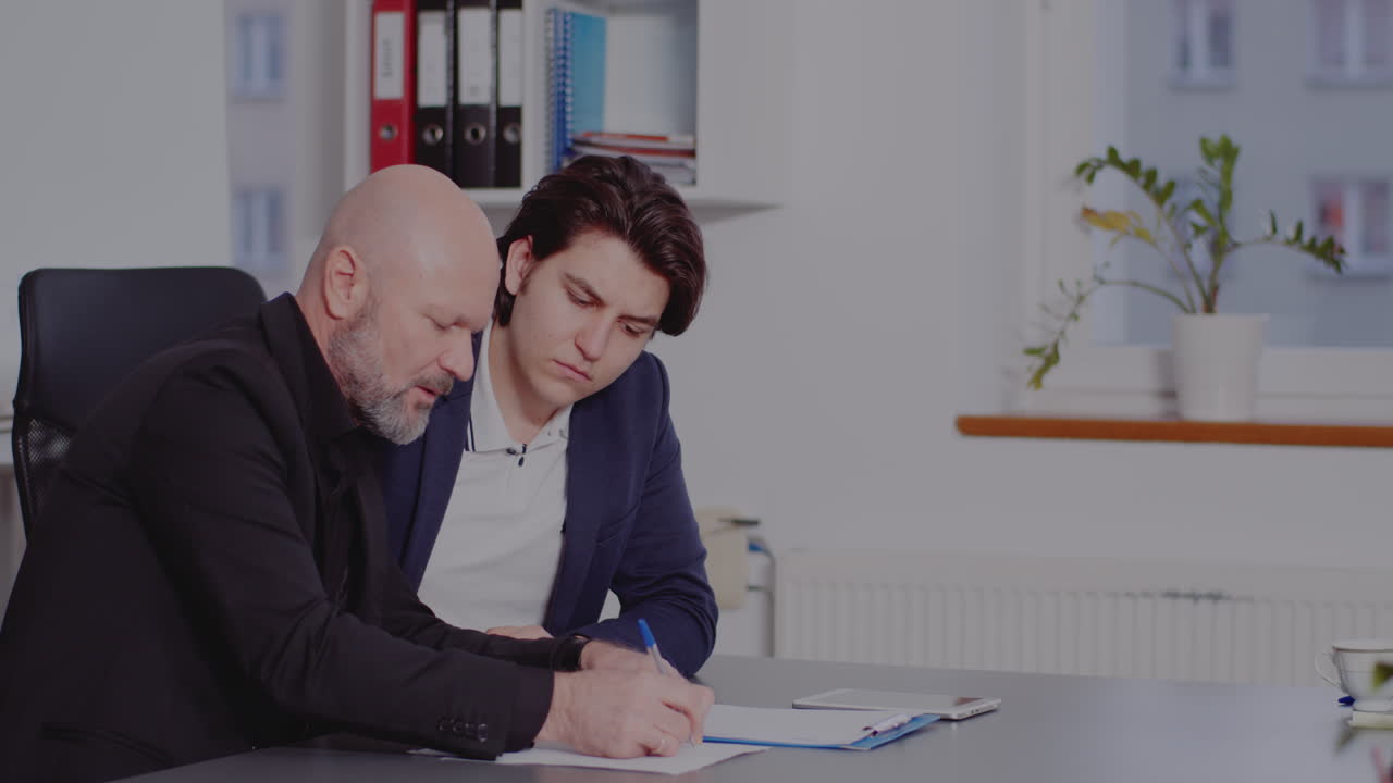Two businessmen signing a document in an office setting