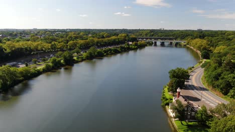 Beautiful-aerial-drone-flight-tracking-the-Schuylkill-River-upstream,-leaving-Philadelphia,-Express-traffic-moving-on-sunny-summer-afternoon