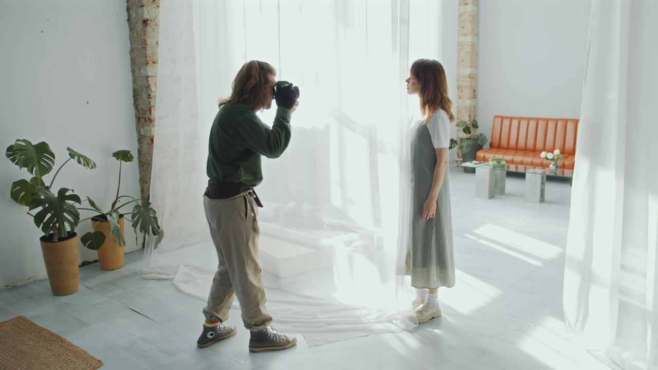Fotografo che scatta foto a una modella in posa dietro una tenda trasparente in studio