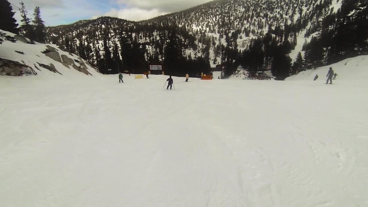 POV, uno snowboarder scivola oltre sciatori e snowboarder mentre scende, superando segnali di sicurezza e avvisi.