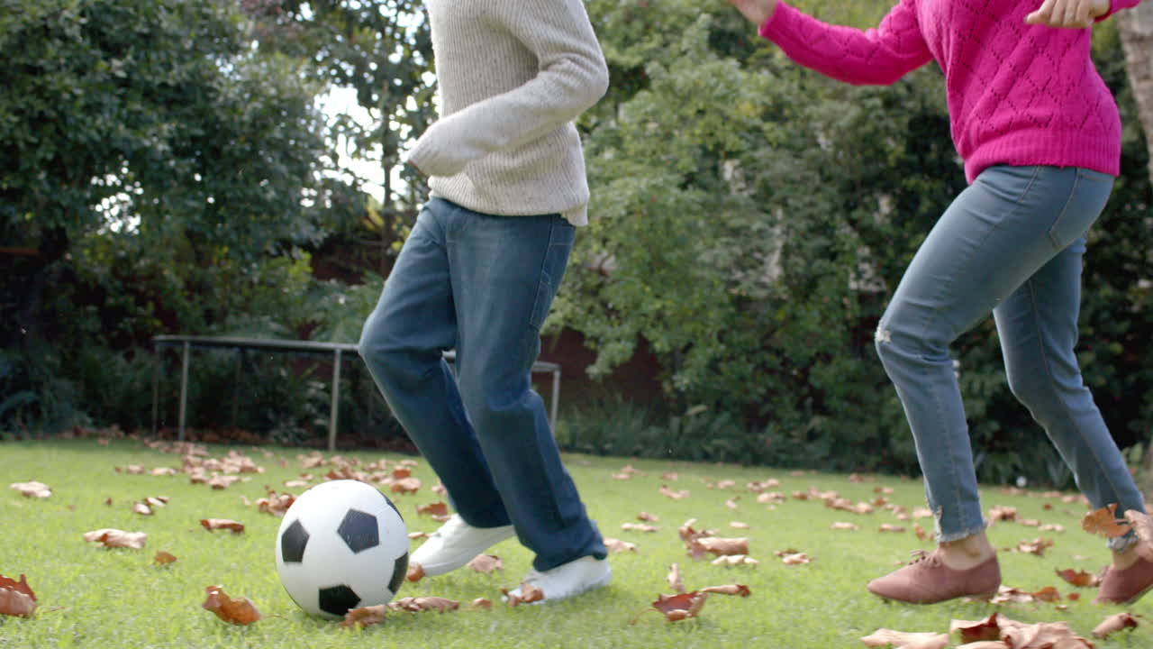 Happy african american mother and son playing football in garden, in slow motion