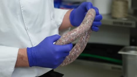 las manos del chef se cierran con guantes azules sosteniendo salchichas de carne fresca en la cocina de un restaurante profesional, preparación de alimentos