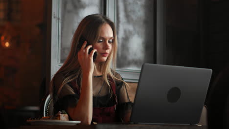 young smiling hipster girl talking with friend via video call via laptop computer while sitting in coffee shop. cheerful female manager having webinar via portable notebook during resting time in cafe