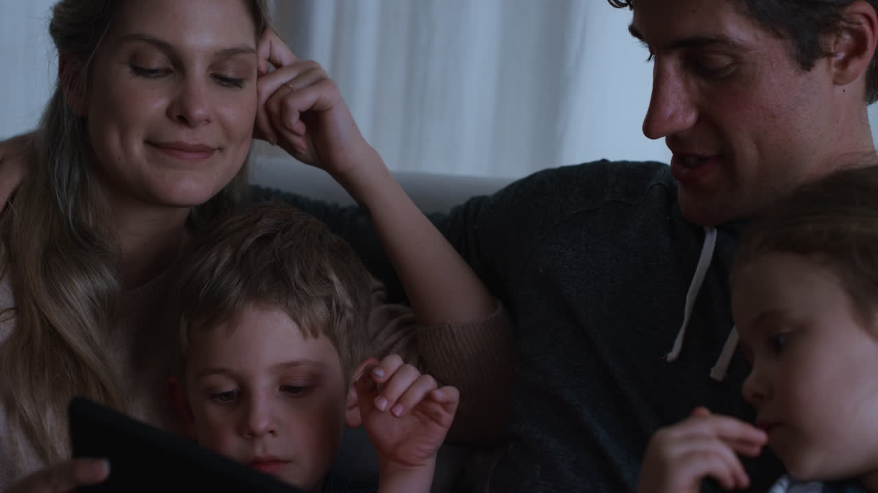 태블릿 컴퓨터를 사용하는 가족 어머니와 아버지는 아이들이 터치 스크린 장치에서 게임을 하는 것을 보고 재미를 배우고 잠자리에 들기 전에 양질의 시간을 즐기고 있습니다. 4k