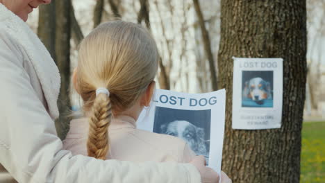 mom soothes the girl who lost the dog on the tree hangs the announcement of the missing puppy