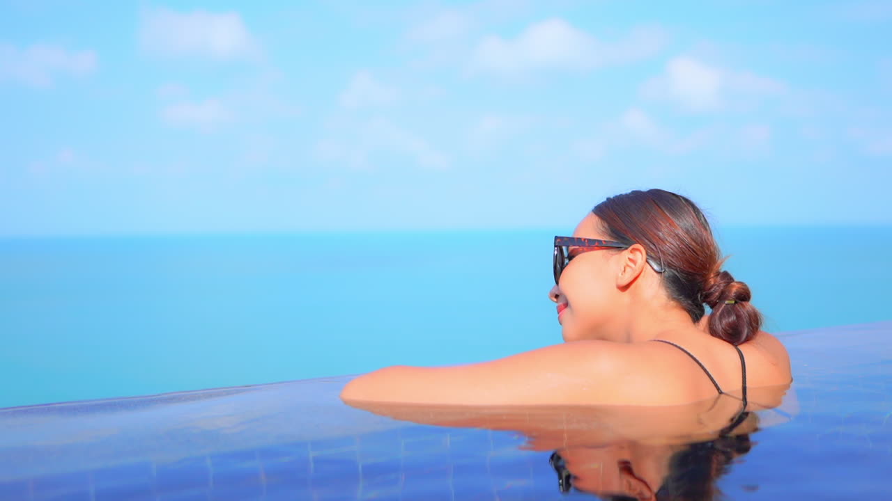 Frau lehnt am Rand eines Infinity-Pools und blickt auf das Meer