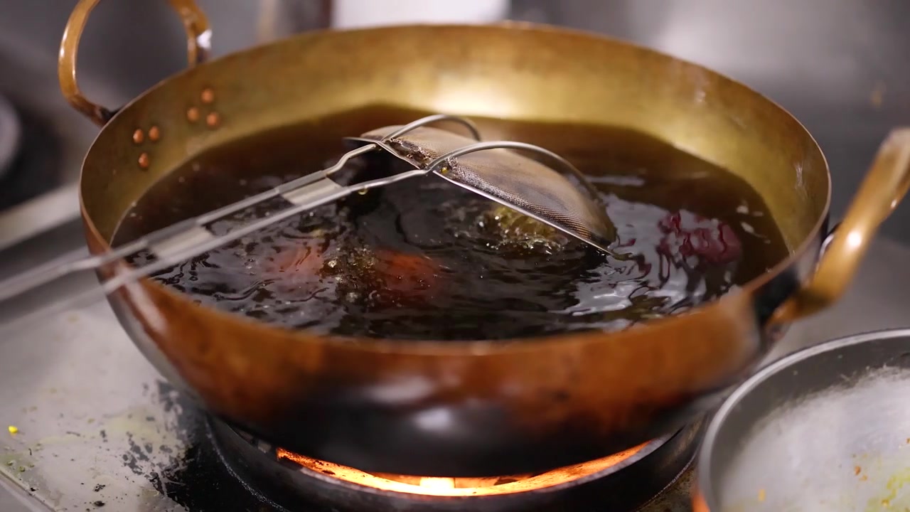 Close-up shot of hands placing samosas into hot oil within a traditional brass wok.