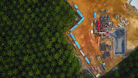 cinematic 4k drone footage of onshore drilling rig equipment structure for oil exploration and exploitation in the middle of jungle surrounded by palm oil trees during sunset and high oil price