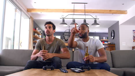 two male friends sit on sofa and watch sports on television