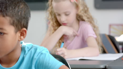 caucasian girl with curly blonde hair is focused on writing in a classroom at school