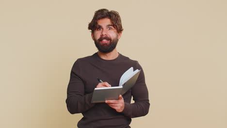nachdenklicher geschäftsmann macht notizen und schreibt gedanken mit einem stift in ein tagebuch auf beige hintergrund auf