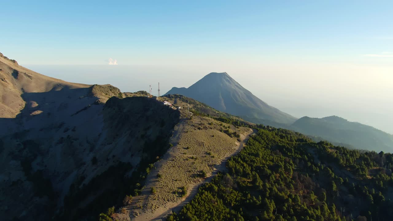 Slow tilt up aerial overlooking trek leading to Las Antenas in the Nevado de Colima National Park with the active Colima volcano in the background
