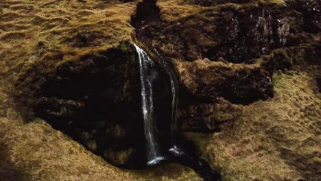 Aerial-view-of-a-stream-flowing-down-a-waterfall-in-Iceland,-in-winter