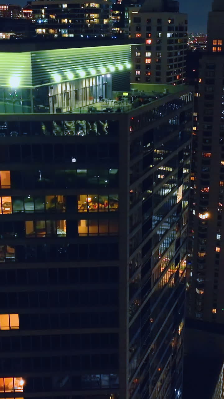Night aerial view of the roof of a skyscraper in downtown Chicago. The building with night lights and reflections in the facade. Vertical video