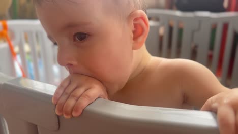 funny baby boy playing with his hand and mouth, playpen awake time in a nursery