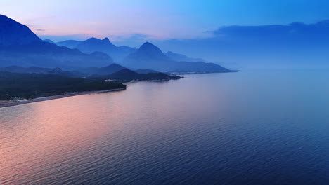 pink light coloring the waterscape of the seascape at sunset time. silhouettes of the mountains in the haze at backdrop