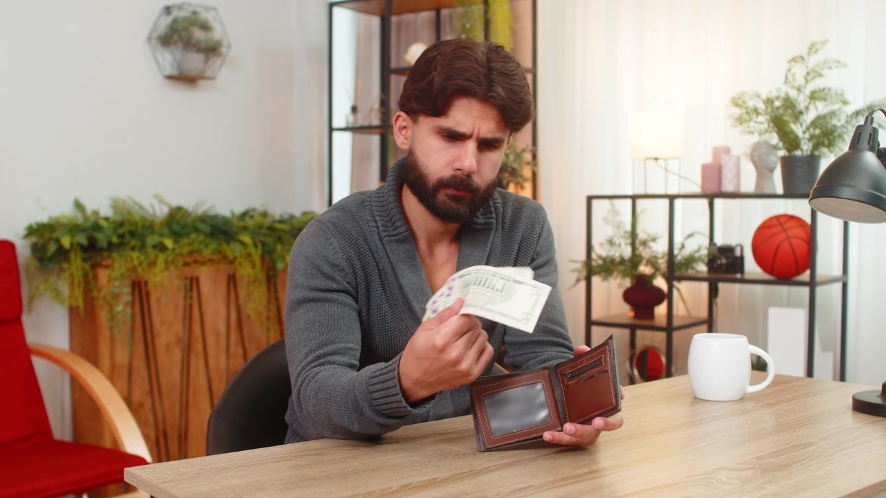 Hombre indio mira en su cartera, solo ve monedas, de humor infeliz, deudas, facturas vencidas, salario bajo y bajas ganancias
