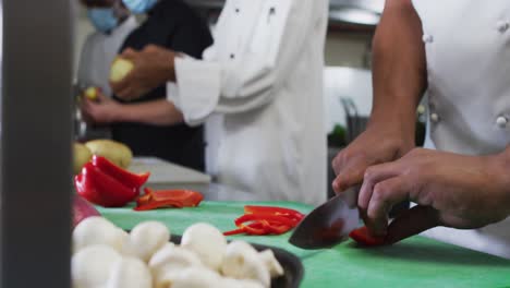 Sección-Media-De-Un-Grupo-Diverso-De-Chefs-Cortando-Verduras-En-La-Cocina-Del-Restaurante.