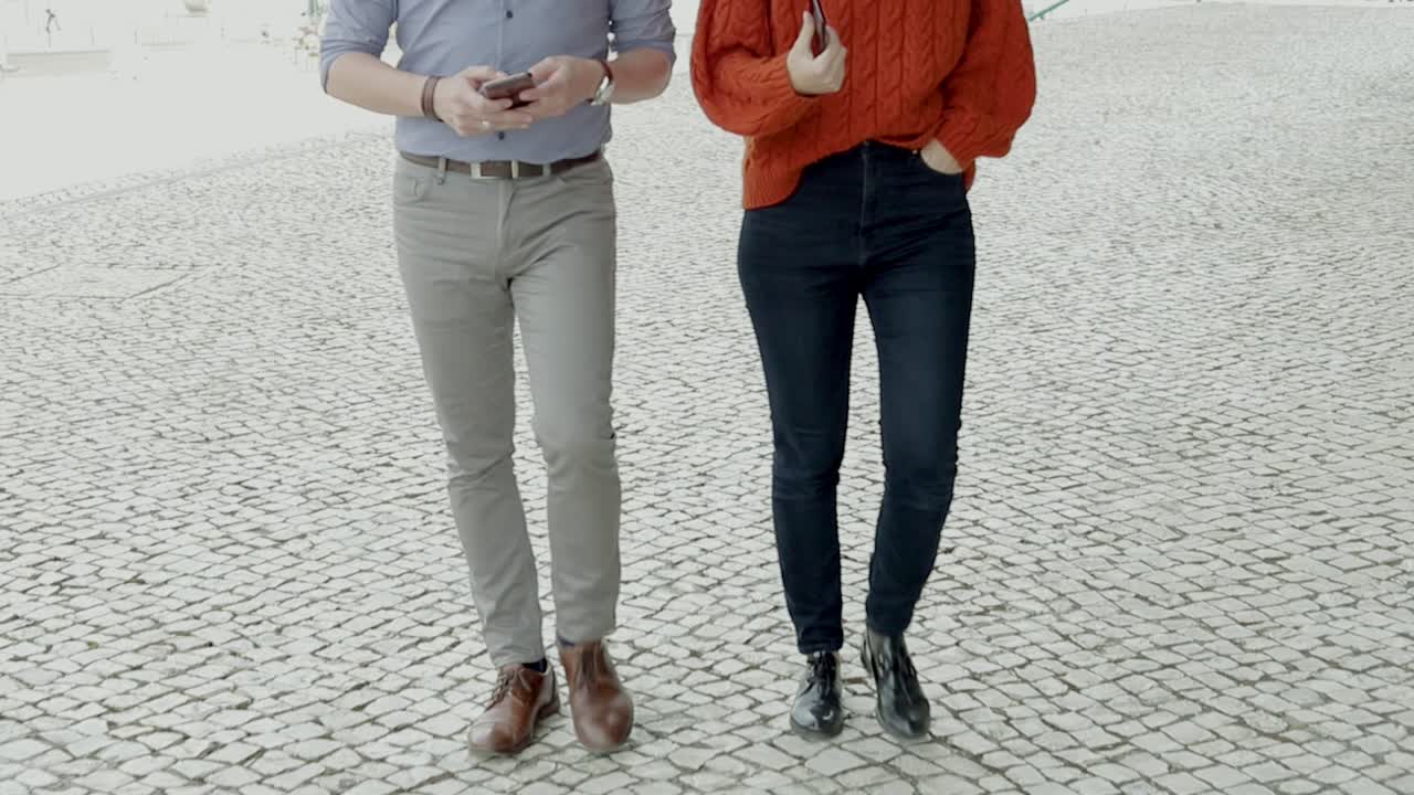 sección baja de una pareja con teléfonos inteligentes caminando por la calle