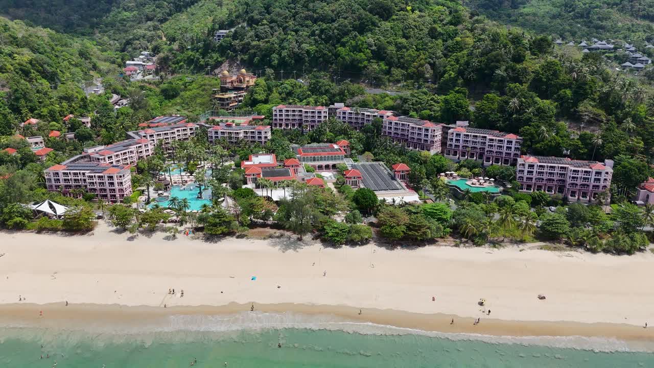 Drone footage captures a scenic flyover of a lush Phuket resort, showcasing vibrant greenery, sandy beaches, and turquoise pools