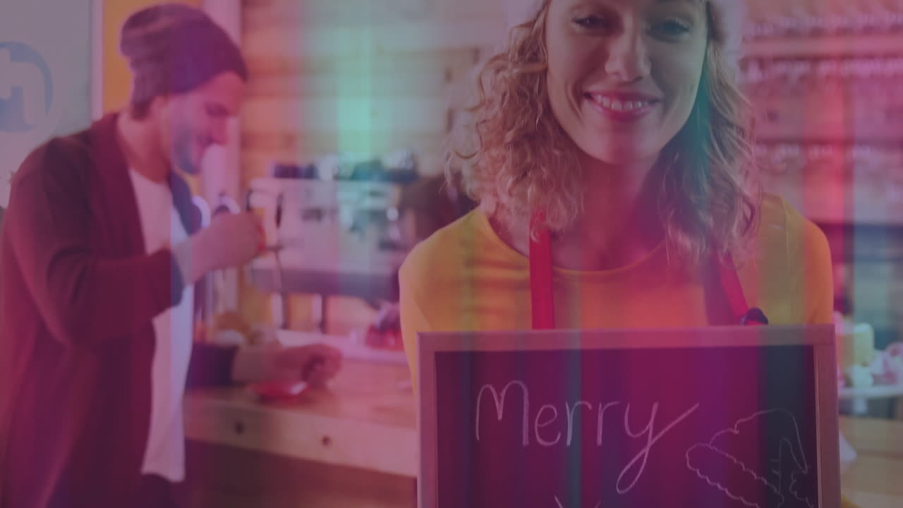 Holding Merry X-mas chalkboard, woman in cozy cafe with barista in background