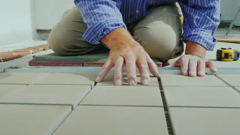 A-Man-Is-Laying-Tiles-On-The-Floor-Only-Hands-Are-Visible-In-The-Frame