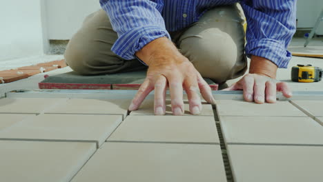 a man is laying tiles on the floor only hands are visible in the frame