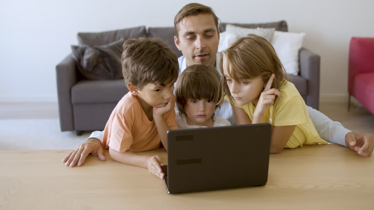 padre alegre leyendo cuentos a niños pensativos desde la computadora portátil