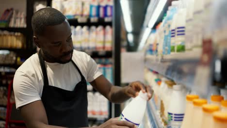 of a black man in a white t-shirt and black apron inspecting tvoar at a dairy counter. video filmed in high quality