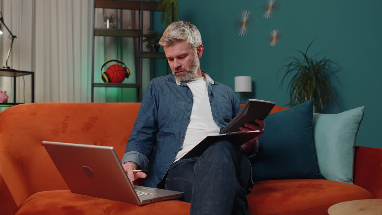 Middle-aged business man working with laptop computer and documents planning expenses budget at home