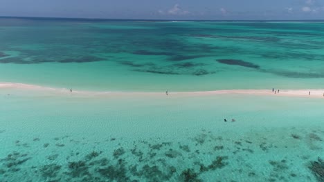 aerial shot people walk on white sand tropical sandbank surrounded by shades of blues