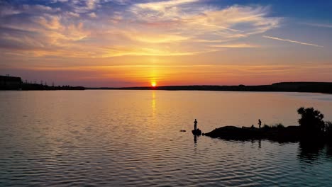 silhouette of a fisherman with fishing rod standing on stone near the river at sunset. evening background over the water and people having great time at the river. aerial view.