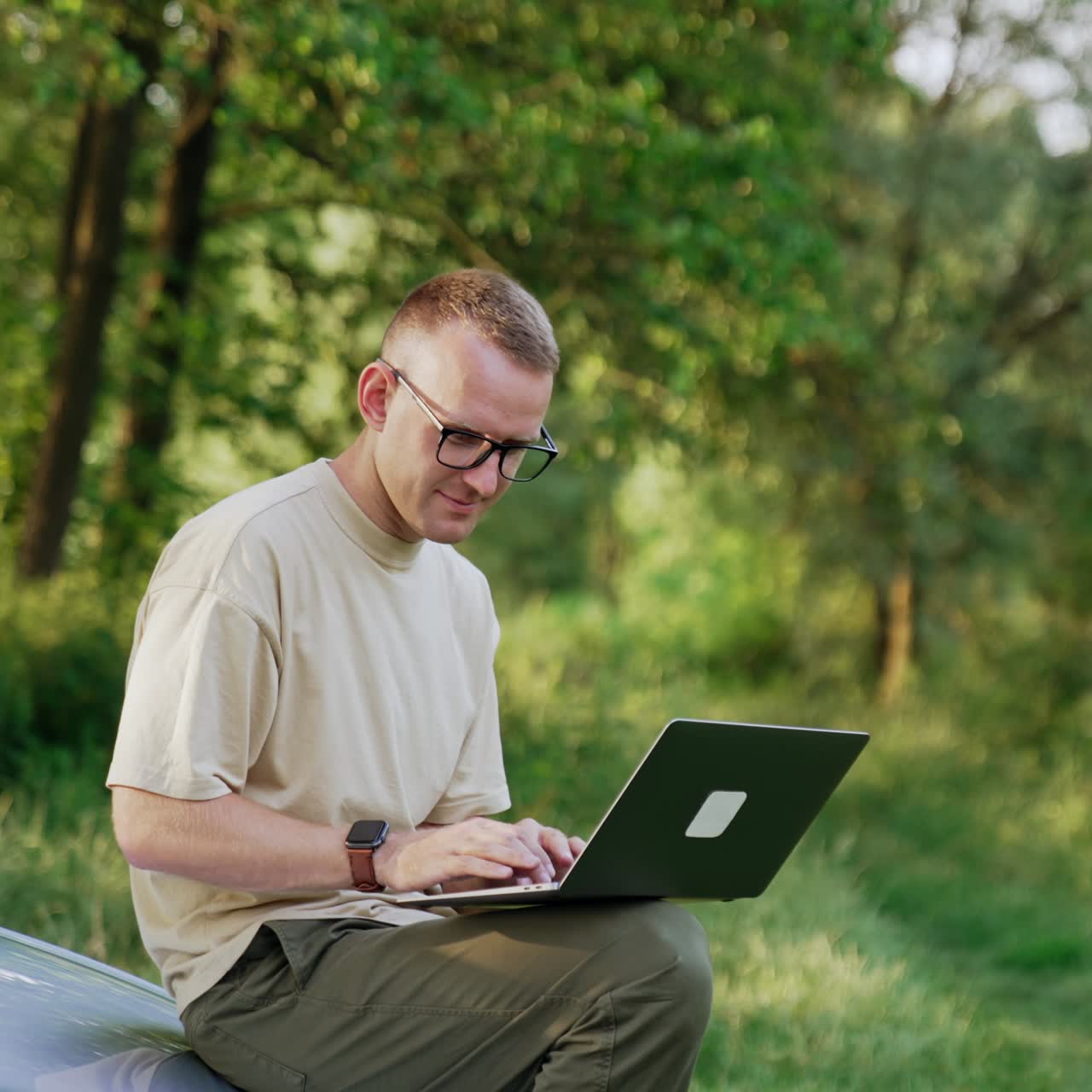 Busy man working in the natural surroundings. Freelancer looks at laptop sitting on the car