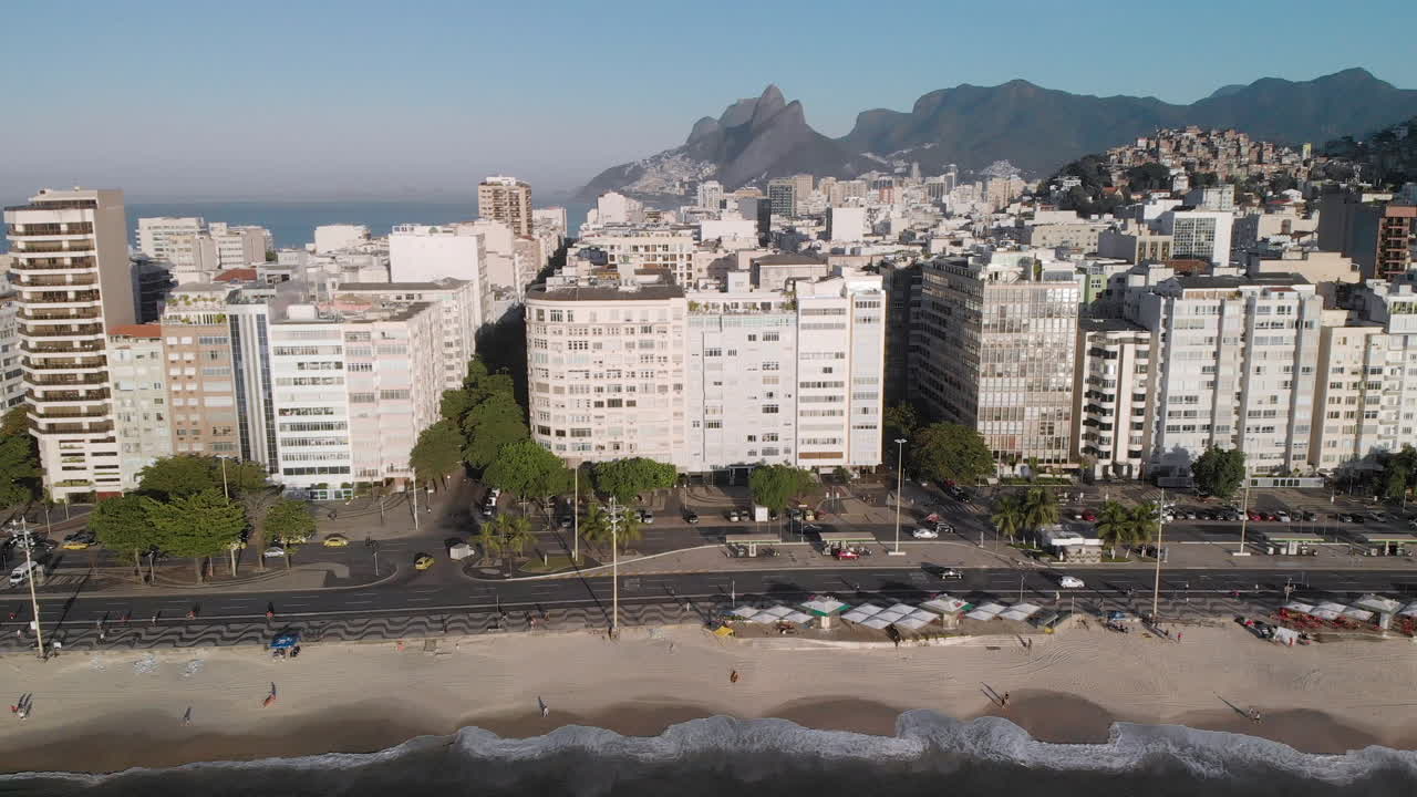 inclinación aérea hacia arriba que revela la playa de copacabana, el bulevar y el vecindario vistos desde el océano con ipanema de fondo y la montaña de dos hermanos contra un cielo azul claro