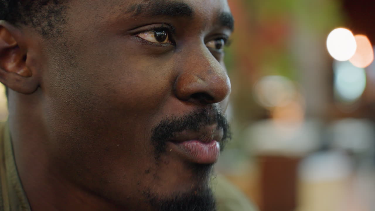 Close up of man chewing snack with warm smile on face, blurred indoor background with soft bokeh lights, lifestyle moment showing casual dining