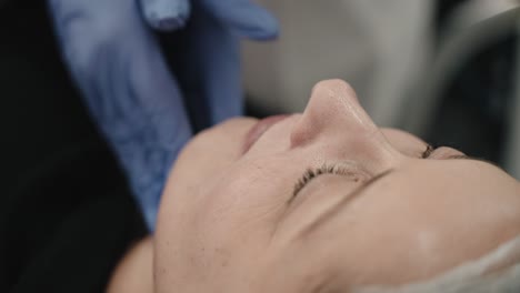 primer plano de una mujer recibiendo un tratamiento facial de un profesional con guantes azules