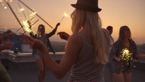 The-young-female-in-the-hat-beautifully-moves-her-hands-in-a-dance-with-big-bengal-light.-She-is-on-the-party-with-her-friends-on-the-roof.