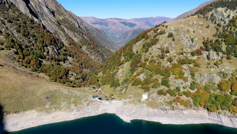 Muro-De-La-Presa-Lac-D&#39;oô-Y-Cabañas-De-Cuidadores-En-Los-Pirineos-Franceses-Durante-El-Día,-Toma-Aérea-De-Aproximación-Alta