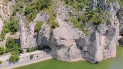 aerial arc footage of beautiful cliffs with road tunnel surrounded by lake