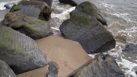 Line-of-Large-Solid-Boulders-on-the-beach-lined-out-into-the-sea-on-Waxham-Sands-beach,-Norfolk,-UK