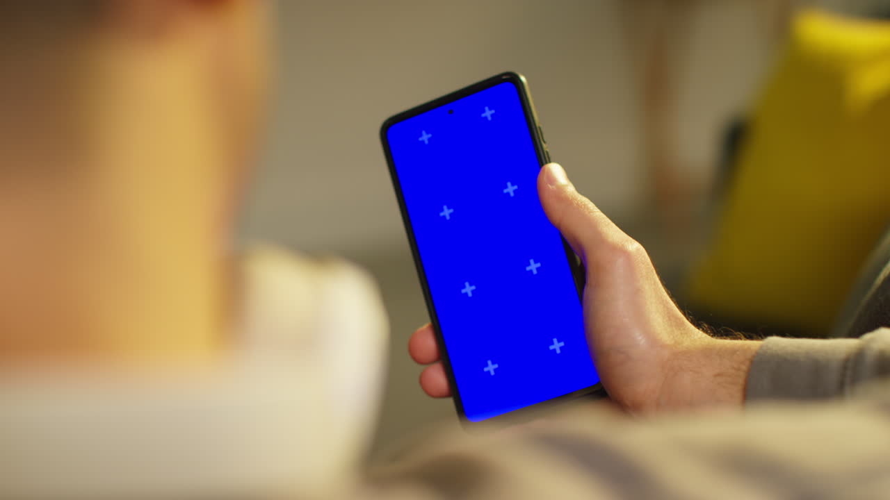 집에서 저녁을 보내고 소파에 앉아 블루 스크린 드폰 1을 보고 있는 남자의 어깨