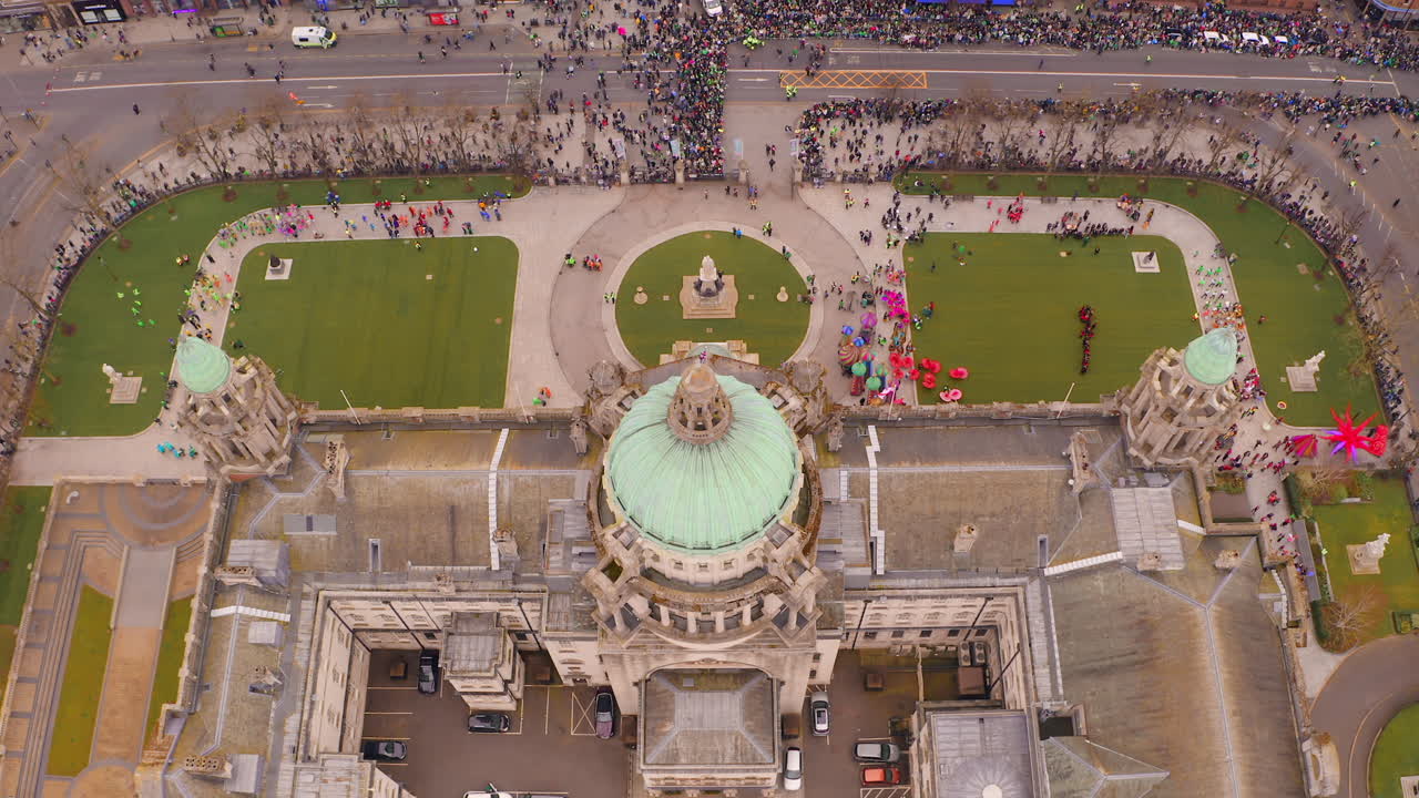 Static aerial view directly above Belfast City Hall showing crowds gathering along streets awaiting the start of St. Patrick's Day parade festivities