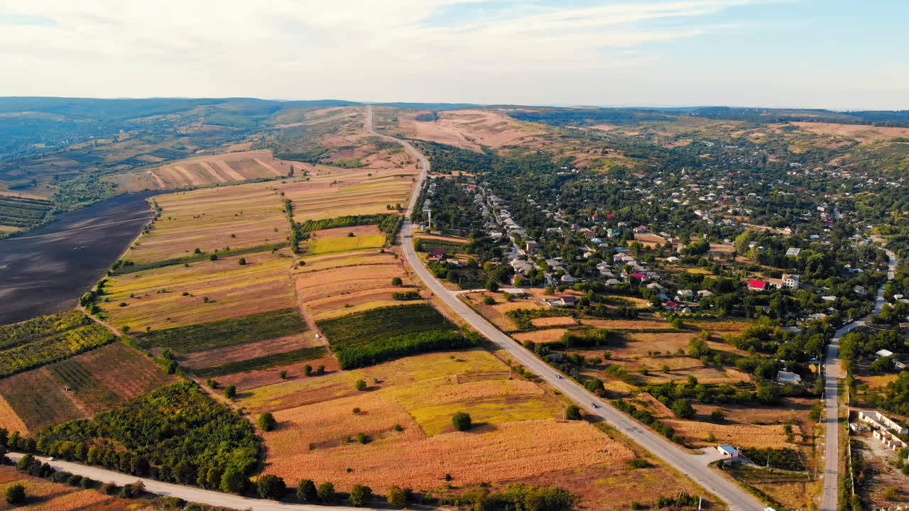Aerial drone view of a crossroads with moving cars in highland. Small village and green hills on background. Sunny day. Balti, Moldova