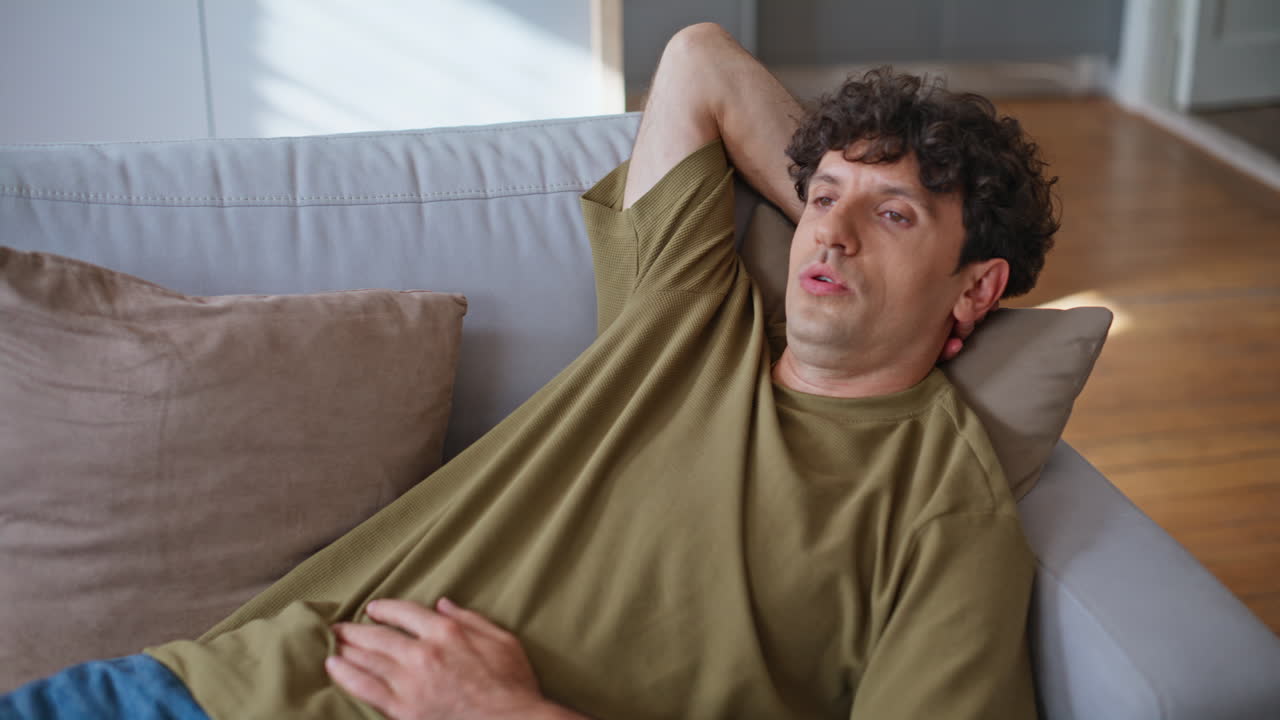 Closeup brunette falling couch feeling relaxed at home. Tired man taking rest