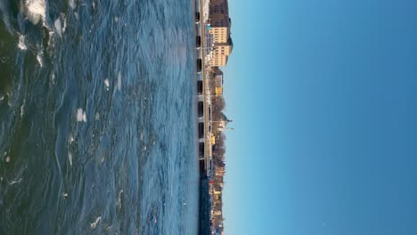 Stockholm's-Skeppsbron-and-Nationalmuseum,-blue-water-with-ice-floes,-sunny-day,-vertical-shot