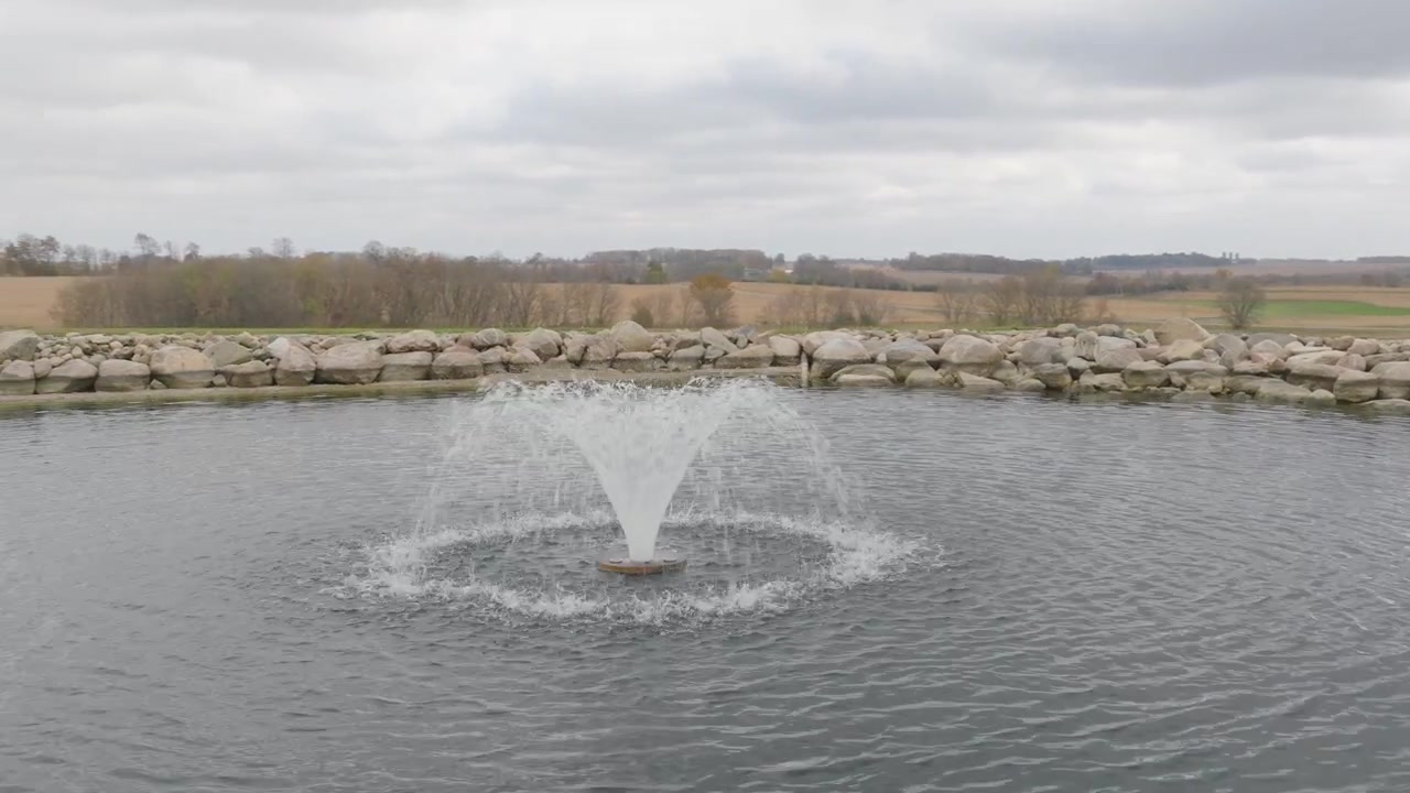 Fontana serena che spruzza acqua in uno stagno rurale con vista panoramica sulla campagna