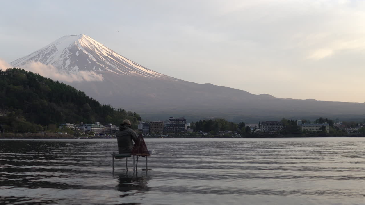 toma amplia de mano de un pescador sentado en el agua del lago kawaguchiko con mt