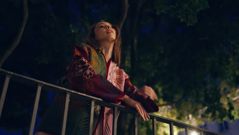 chica inclinada sobre las barandillas del parque posando al crepúsculo de cerca. mujer de pie en el jardín